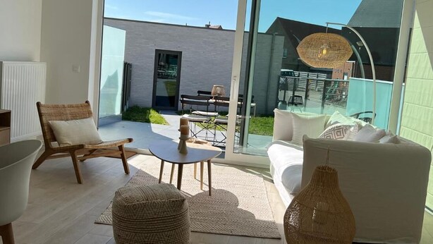 Ein modernes Wohnzimmer mit einer Couch, einem Sessel, einem Tisch und einer großen Glasdoor, die zu einem Außenbereich führt.