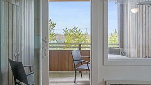Una habitación con puerta corrediza de vidrio que da a un balcón exterior con terraza de madera y una silla.