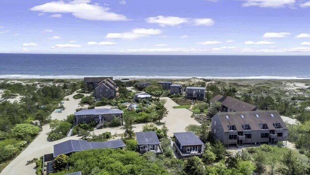 Una zona residencial costera con varias casas, vista despejada del océano y una playa de arena.