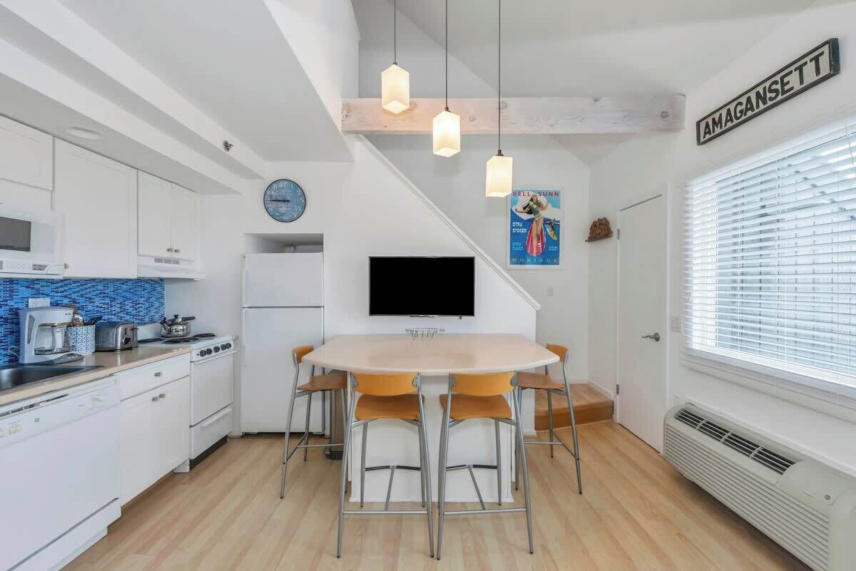 Une cuisine moderne avec des meubles blancs, un îlot central et un coin repas comprenant une table ronde et des chaises.