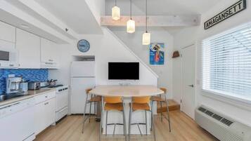 Une cuisine moderne avec des meubles blancs, un îlot central et un coin repas comprenant une table ronde et des chaises.