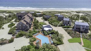 An aerial view of a coastal hotel with multiple buildings, a swimming pool, and a beach in the background. - Unit 1825: 1-Bedroom with Loft | 2nd Floor-Partial Ocean View | Dunes East (Amagansett)