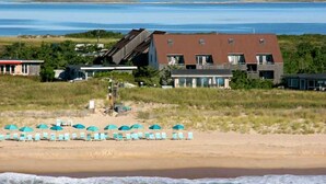 A coastal property with beachside amenities including lounge chairs and umbrellas, a staircase leading to a building, and a view of the sea. - Unit 1825: 1-Bedroom with Loft | 2nd Floor-Partial Ocean View | Dunes East (Amagansett)
