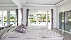 Quarto moderno com uma cama grande, vista para uma piscina e porta de vidro que dá para uma área externa.
