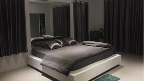 Quarto moderno com cama grande, cortinas escuras e um espelho.