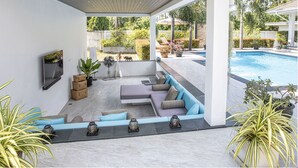 Uma área de estar coberta ao ar livre, com uma piscina ao fundo.