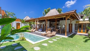 A poolside area with lounge chairs, a covered seating area, and a clear blue sky. - Villa Namu by Alfred in Bali (Seminyak)