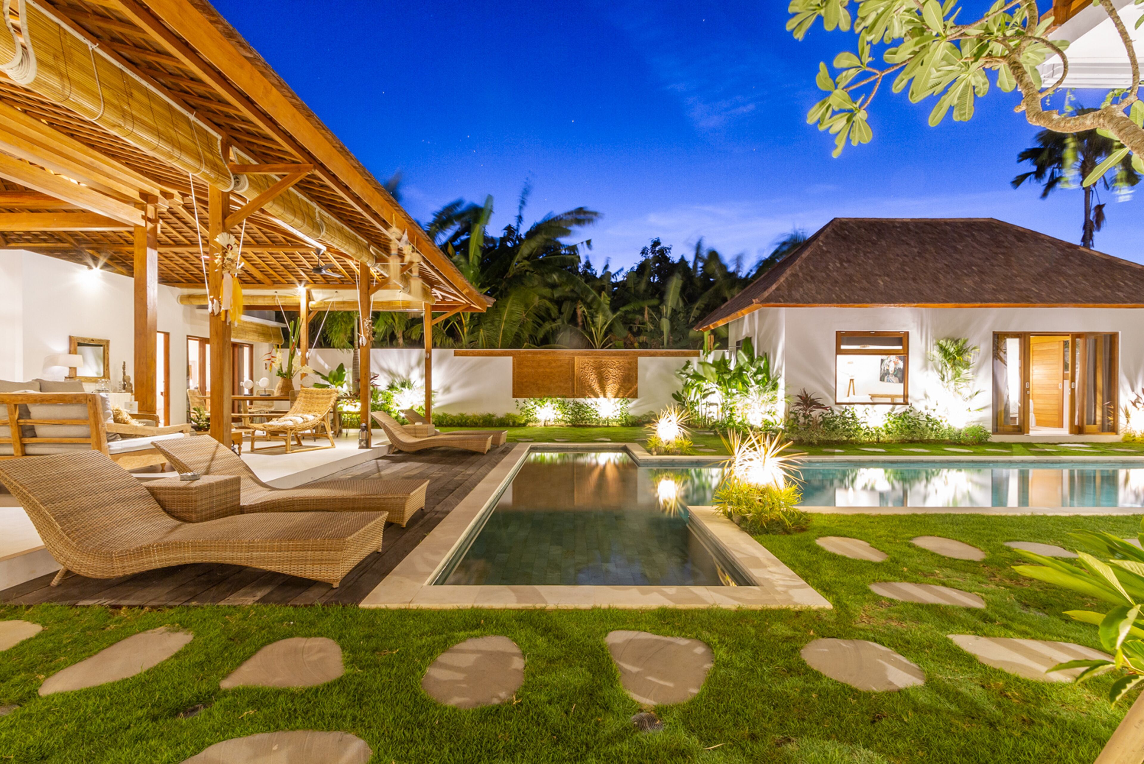 A pool area with lounge chairs, a small pool, and a building with large windows.