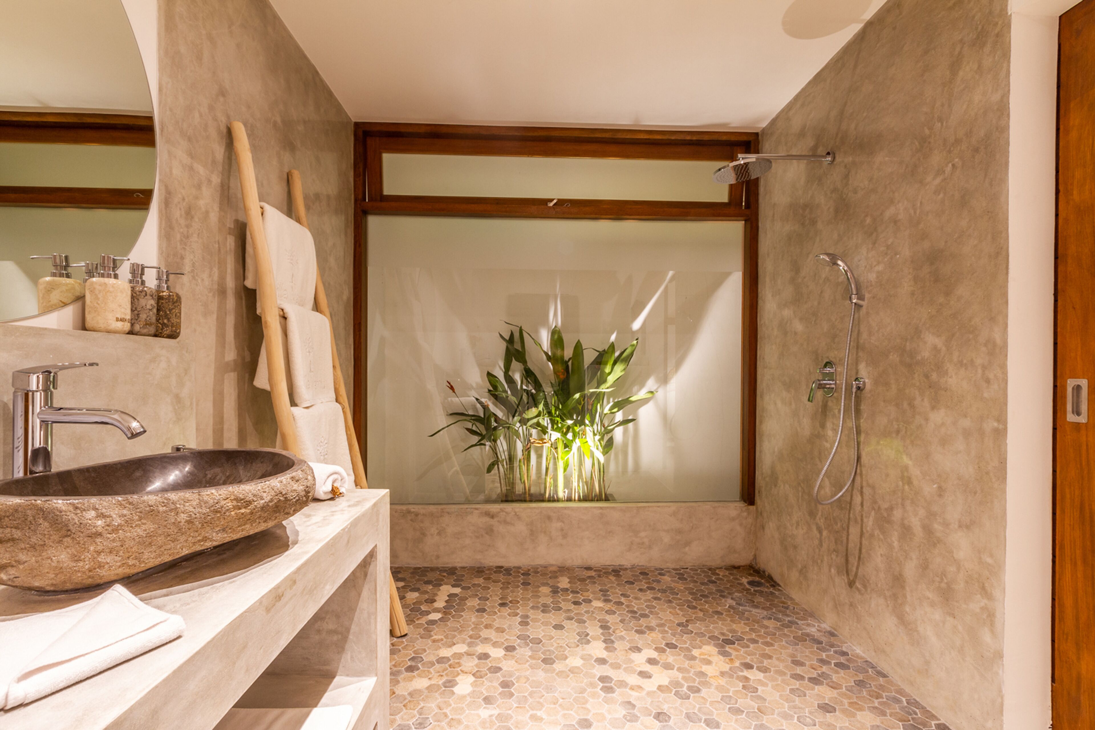 Um banheiro moderno com pia de pedra, móvel de vaidade em madeira, espelho grande, chuveiro com porta de vidro e um vaso de planta.