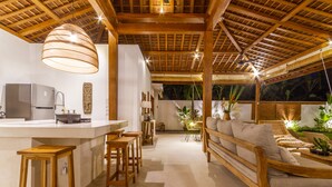 A modern kitchen with a central island, wooden stools, and a seating area with a sofa and chairs. - Villa Namu by Alfred in Bali (Seminyak)