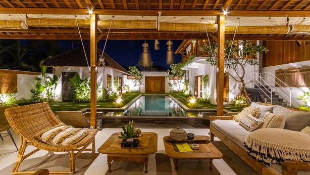 A poolside area with a wooden pergola, lounge chairs, a sofa, and a small table with a plant. - Villa Namu by Alfred in Bali (Seminyak)