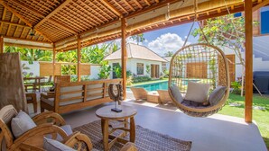 A covered outdoor area with wooden furniture, a hanging chair, and a view of a swimming pool. - Villa Namu by Alfred in Bali (Seminyak)