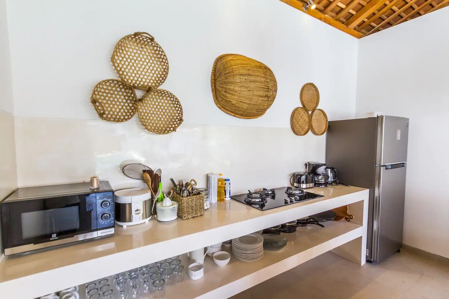 A modern kitchen with a microwave, stove, and refrigerator. There are woven baskets on the wall and a coffee maker on the counter.