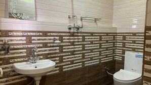 Une salle de bain équipée d’un lavabo, de toilettes et d’une douche. Les murs sont recouverts de carreaux décoratifs formant un motif.