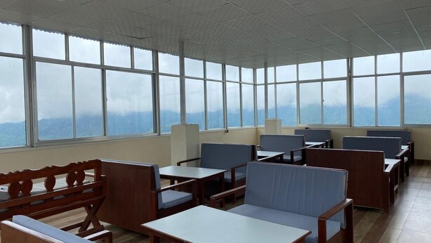 Une pièce spacieuse avec de nombreuses tables et chaises en bois, et de grandes fenêtres offrant une vue sur les montagnes.