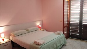 A bedroom with a bed, bedside lamps, a nightstand, a window with blinds, and a door. - VILLA CECILIA/ap. 2: mid in the nature and close to  golden Cilento beaches (Pisciotta)