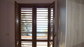 A room with a wooden door with horizontal blinds, a bed with a patterned bedspread, and a white wall with a light switch. - VILLA CECILIA/ap. 2: mid in the nature and close to  golden Cilento beaches (Pisciotta)