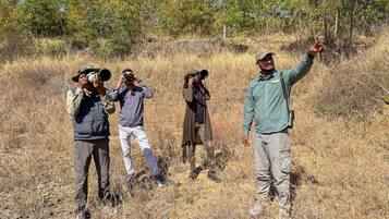 Four individuals in a natural setting with dry grass and trees in the background.