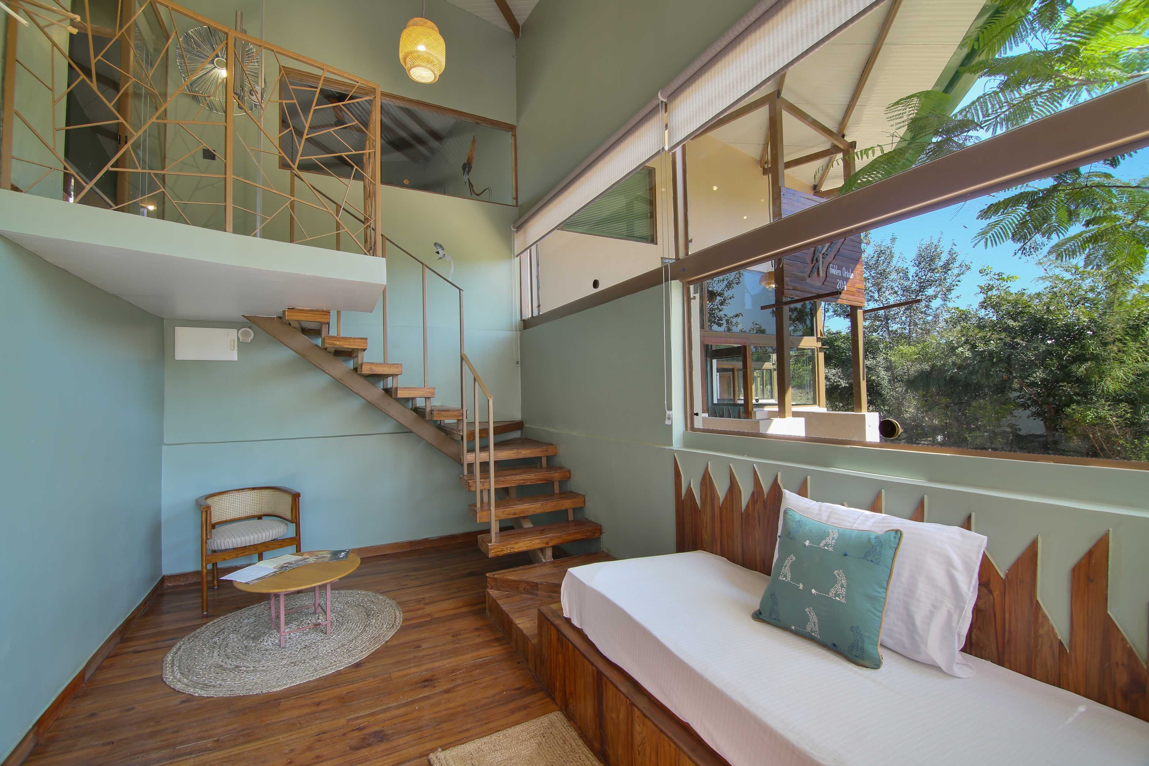 A bedroom with a wooden bed, a chair, a small table, and a staircase leading to an upper level.