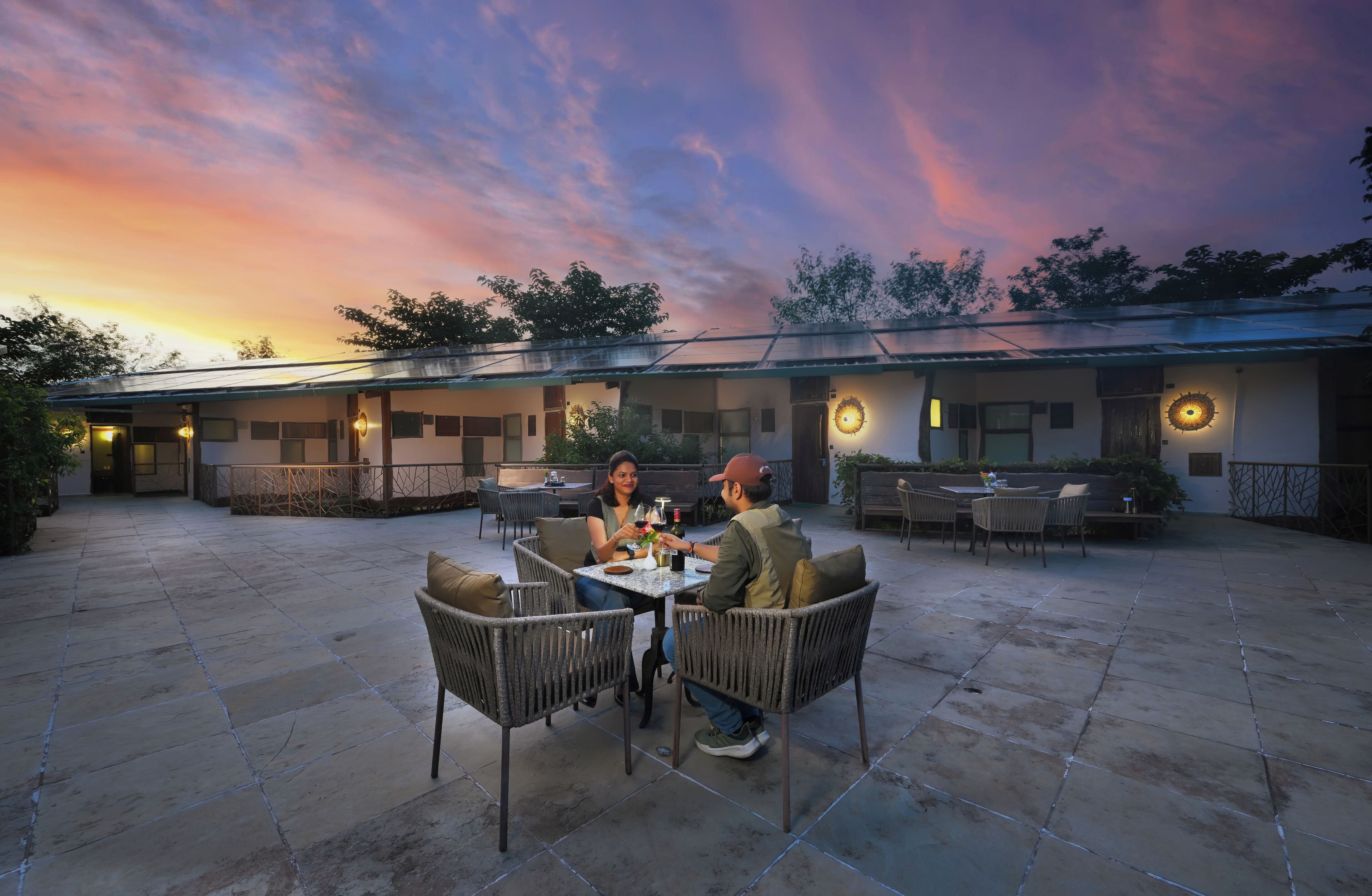 Un patio al aire libre con una mesa y sillas, una zona de estar cubierta y un cielo al atardecer.