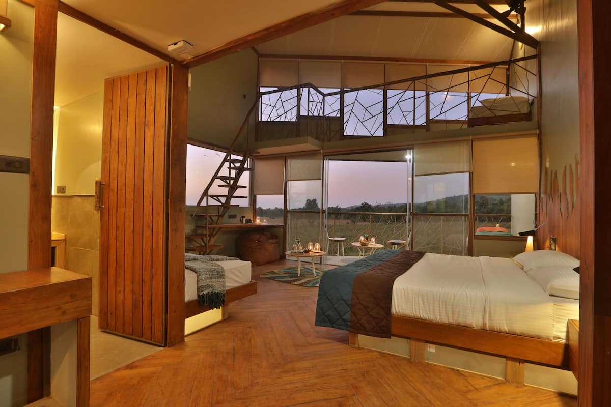 A spacious bedroom with a loft area, wooden flooring, and large windows offering a view of the outdoors.