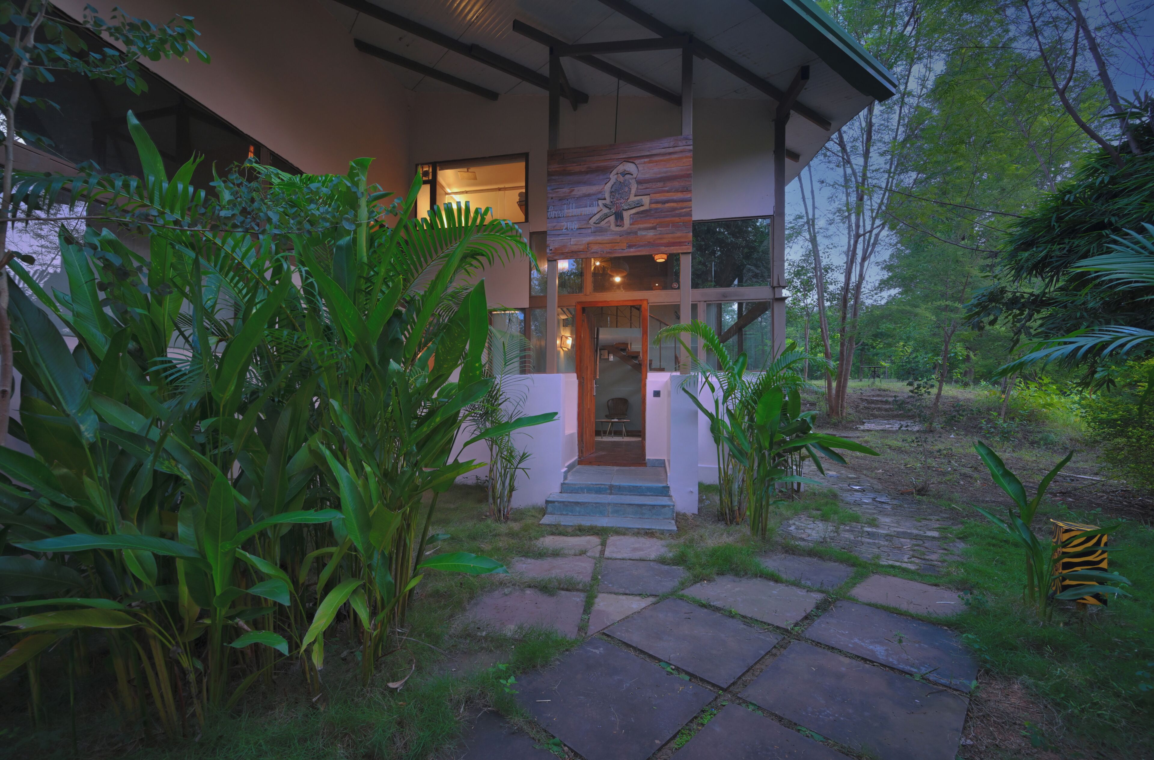 A modern building with a stone pathway leading to the entrance, surrounded by lush greenery.