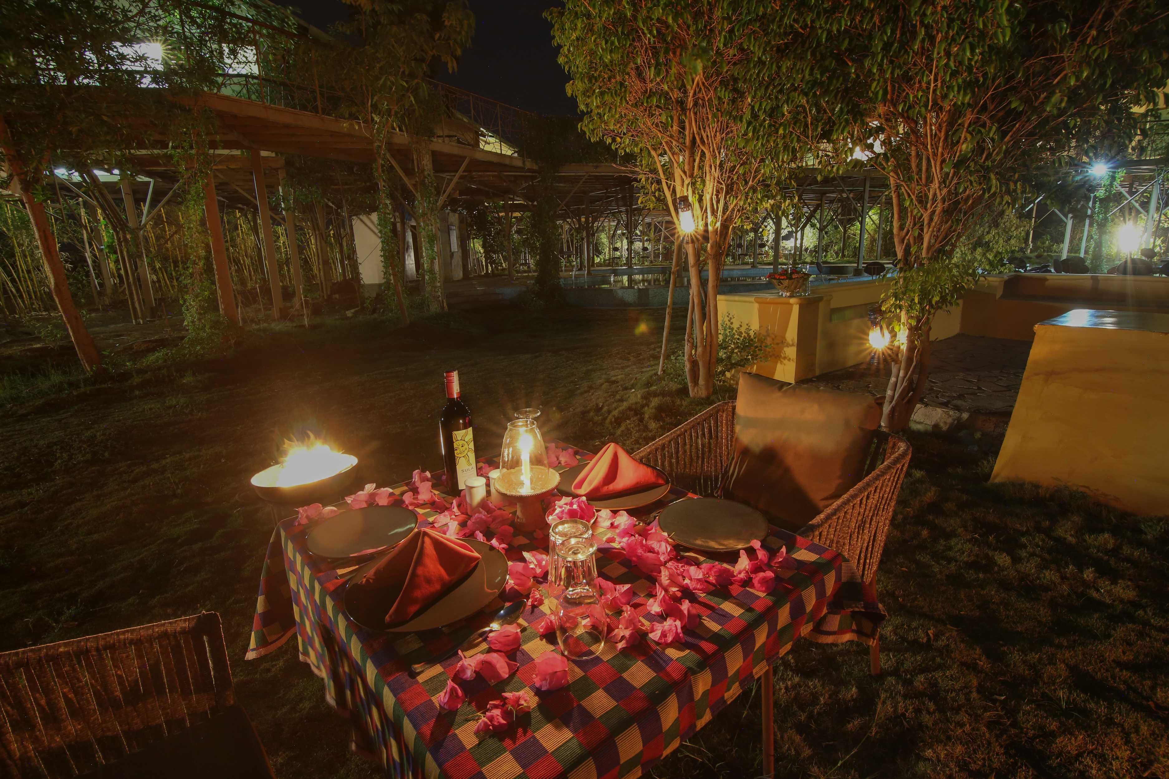 An outdoor dining area with a table set for two, surrounded by chairs, under a pergola with string lights.