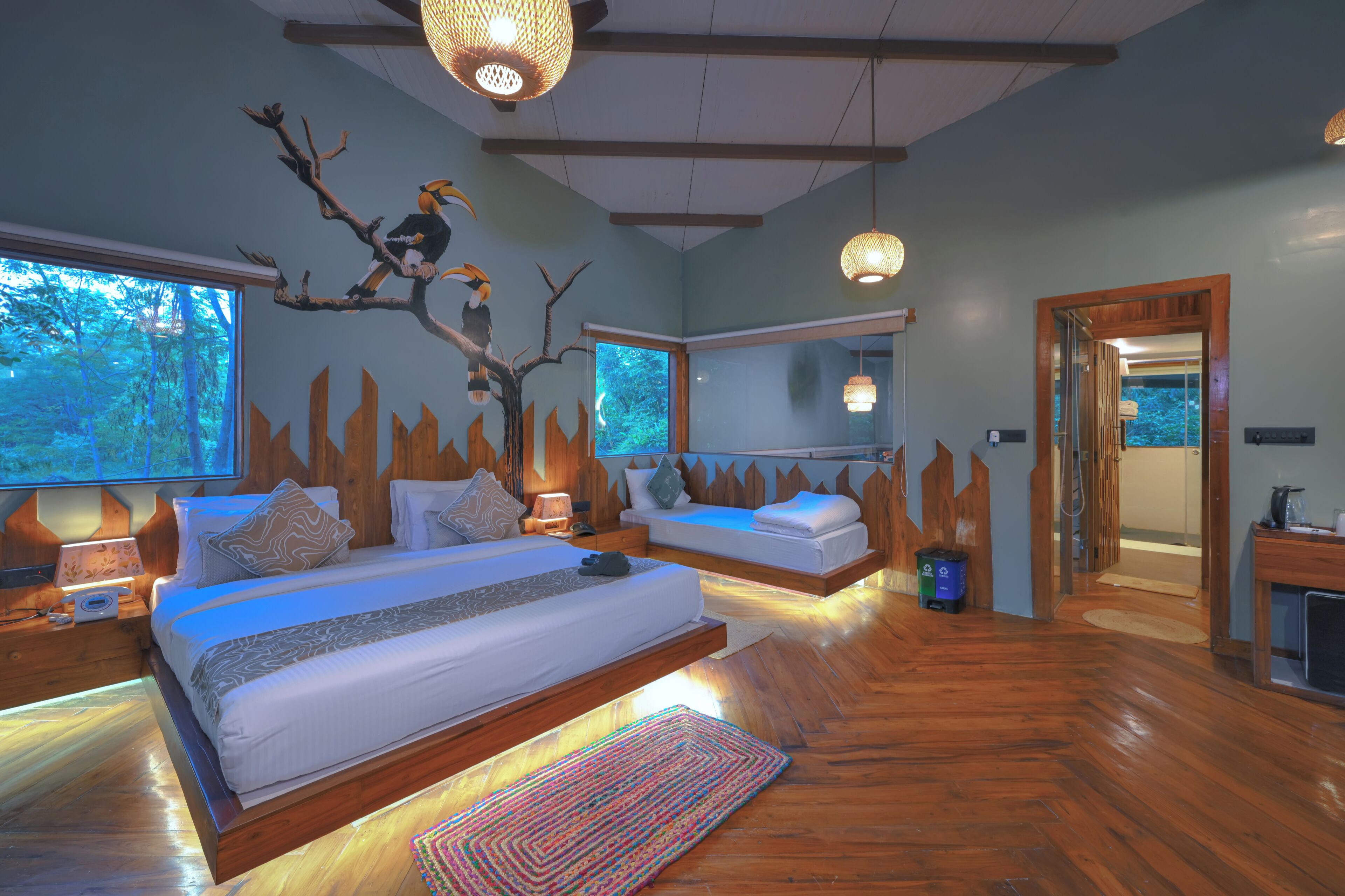 A bedroom with a large bed, a smaller bed, a wooden floor, and a tree branch decoration on the wall.