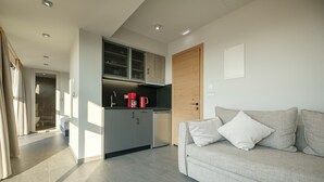 A modern kitchen with a built-in oven, a coffee machine, and a dishwasher. There is a grey sofa with white cushions in the living area. - Sky-High Central Penthouse - 01 (Chania)