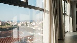 A room with a large window, curtains, and a view of a coastal town. - Sky-High Central Penthouse - 01 (Chania)