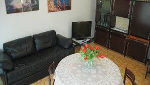 A living room with a black leather sofa, a TV, a table with a vase of red flowers, and two paintings on the wall.