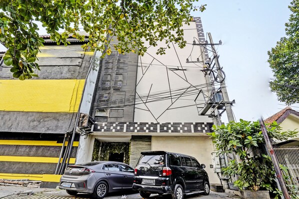 Un bâtiment à la façade jaune et noire, un SUV noir garé devant, et des câbles électriques apparents.