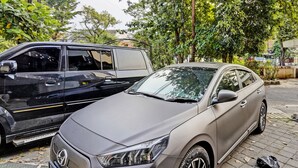 Un coche aparcado en una zona residencial, con árboles y un edificio al fondo.
