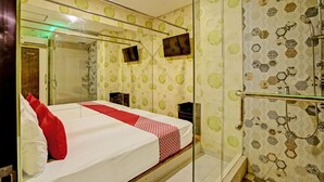 Habitación de hotel con una cama grande, cabina de ducha de vidrio y un espejo.