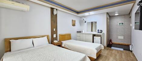 A hotel room with two beds, a desk, a mirror, a small kitchenette, and a ceiling fan.