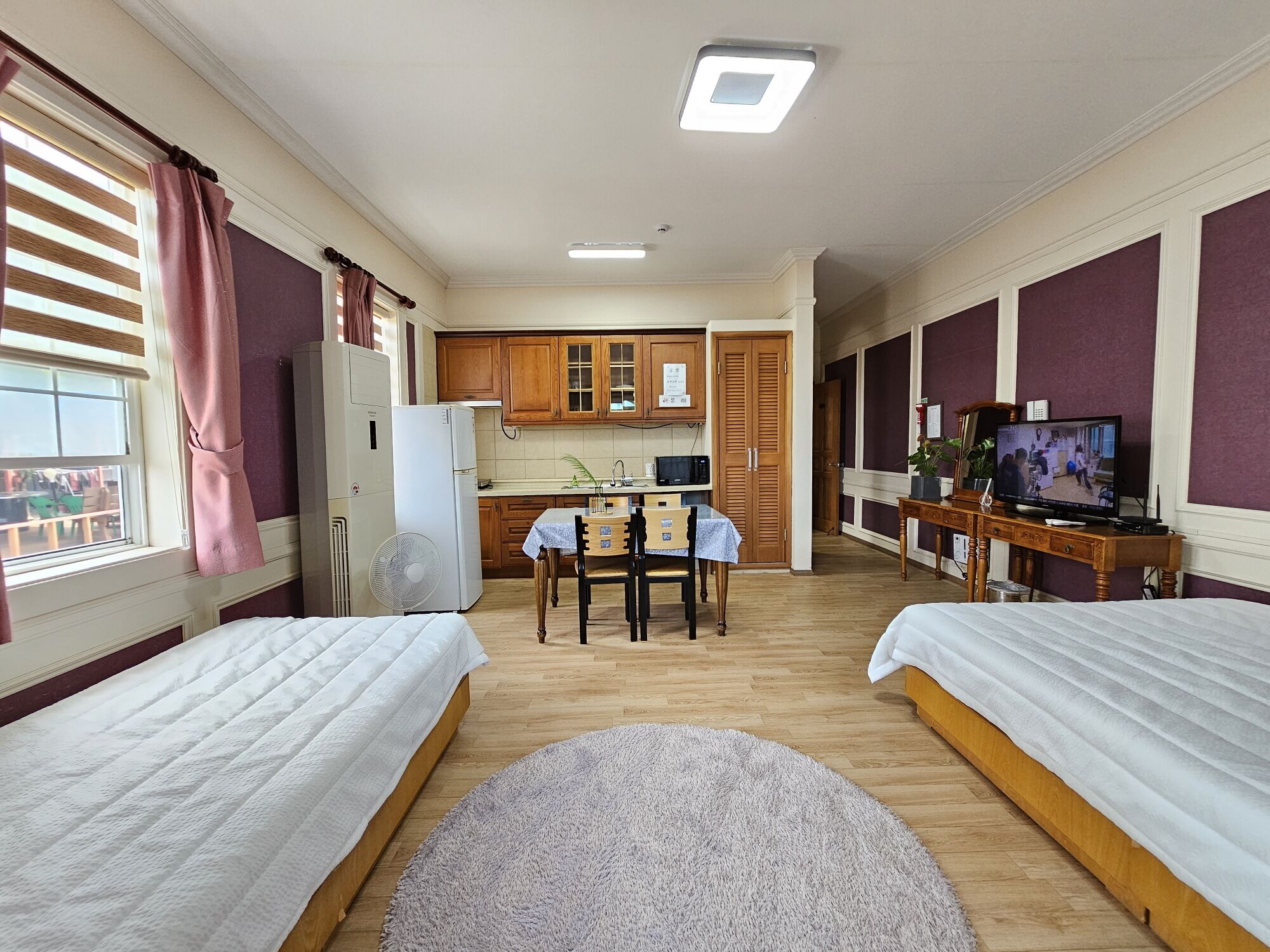 Hotellihuone, jossa on kaksi sänkyä, pieni keittonurkkaus, ruokailutila ja televisio.