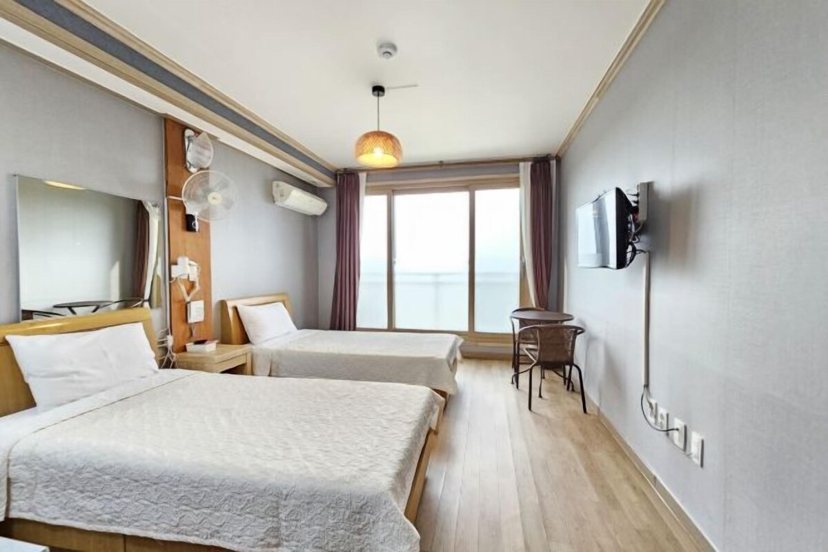 A hotel room with two beds, a TV, a desk, and a large window with a view.
