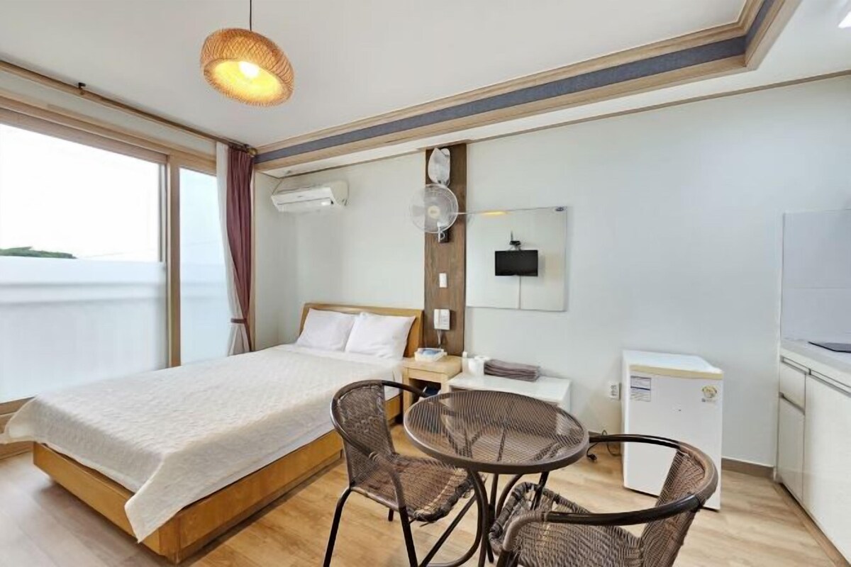 A hotel room with a bed, a small table with chairs, a TV, a mini-fridge, and a window with curtains.