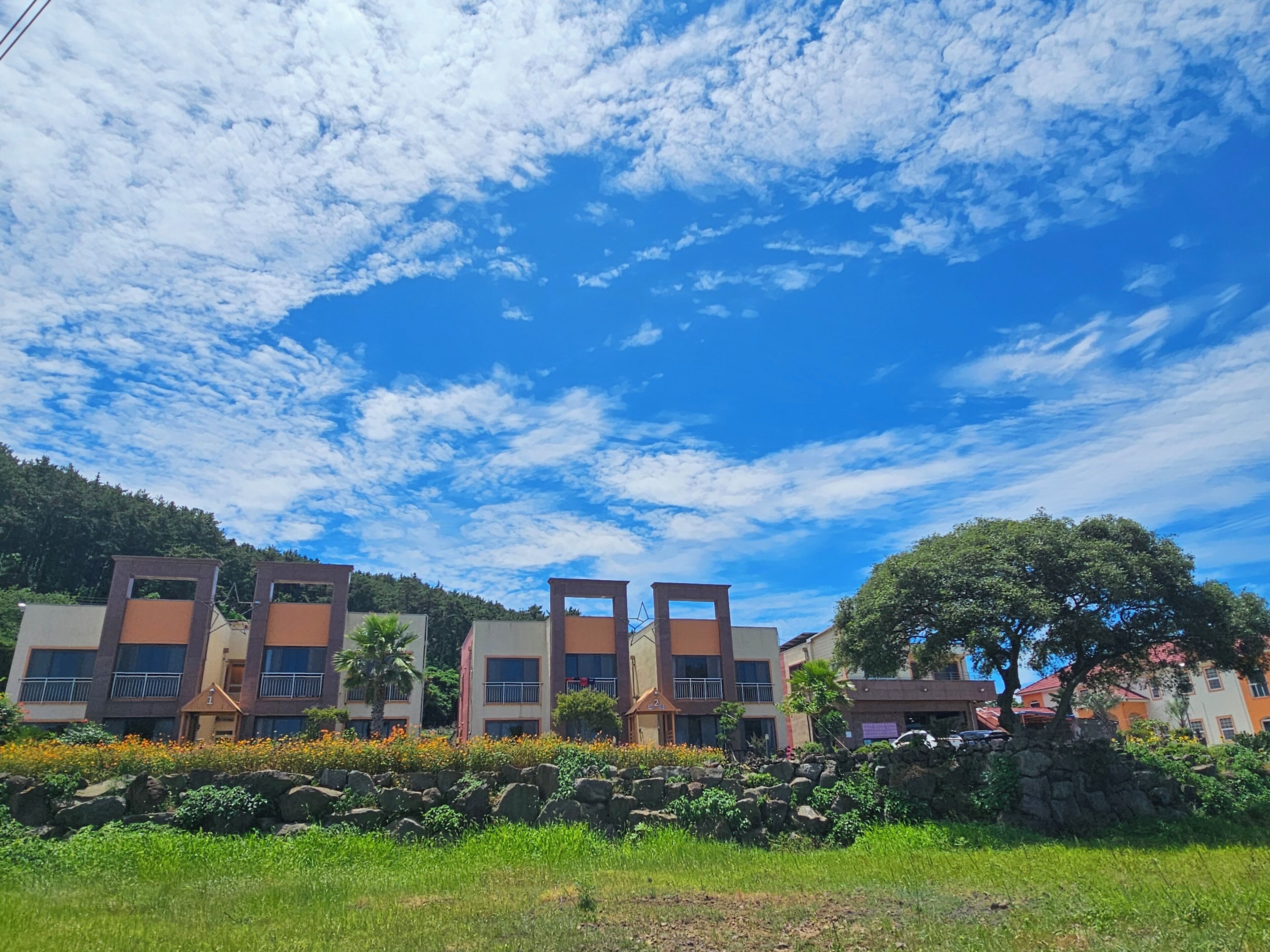 A multi-story building with balconies, a stone wall, and a clear blue sky with clouds.