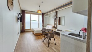A compact hotel room with a bed, a small dining table, a kitchenette, and a large window offering a view. - Red Castle Pension (Jeju City)