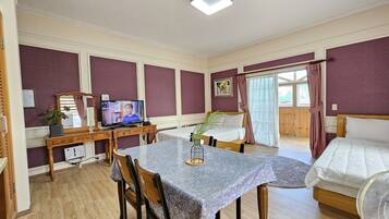 A room with a dining table, chairs, a TV, a bed, and a fan.