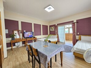 A room with a dining table, chairs, a TV, a bed, and a fan. - Red Castle Pension (Jeju City)