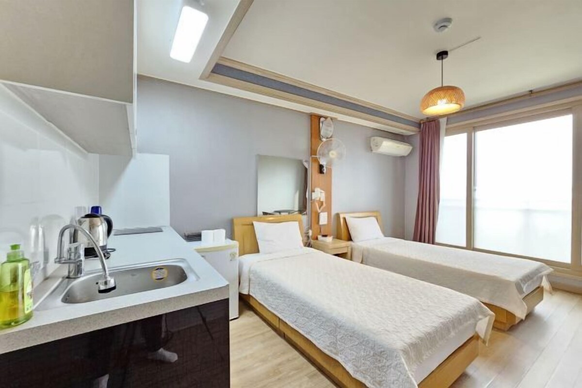 A hotel room with two beds, a sink, a mirror, and a window with curtains.