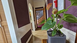 A hallway with a potted plant, wooden flooring, and a staircase in the background. - Red Castle Pension (Jeju City)
