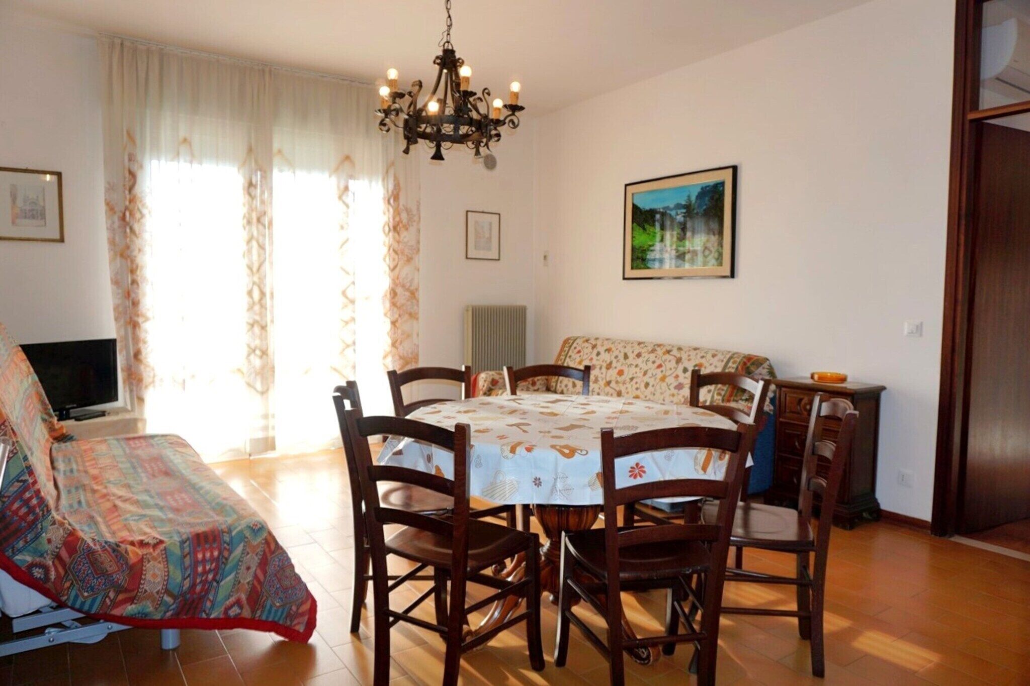 Ein Essbereich mit einem runden Tisch, Holzstühlen, einer Chandelüster, einer Couch und einem Fernseher.