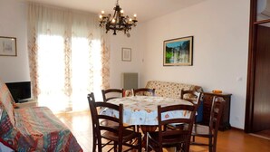 Un coin repas comprenant une table ronde, des chaises en bois, un lustre, un canapé et un téléviseur.