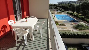 Un balcon avec une table et des chaises, donnant sur une piscine et un jardin.