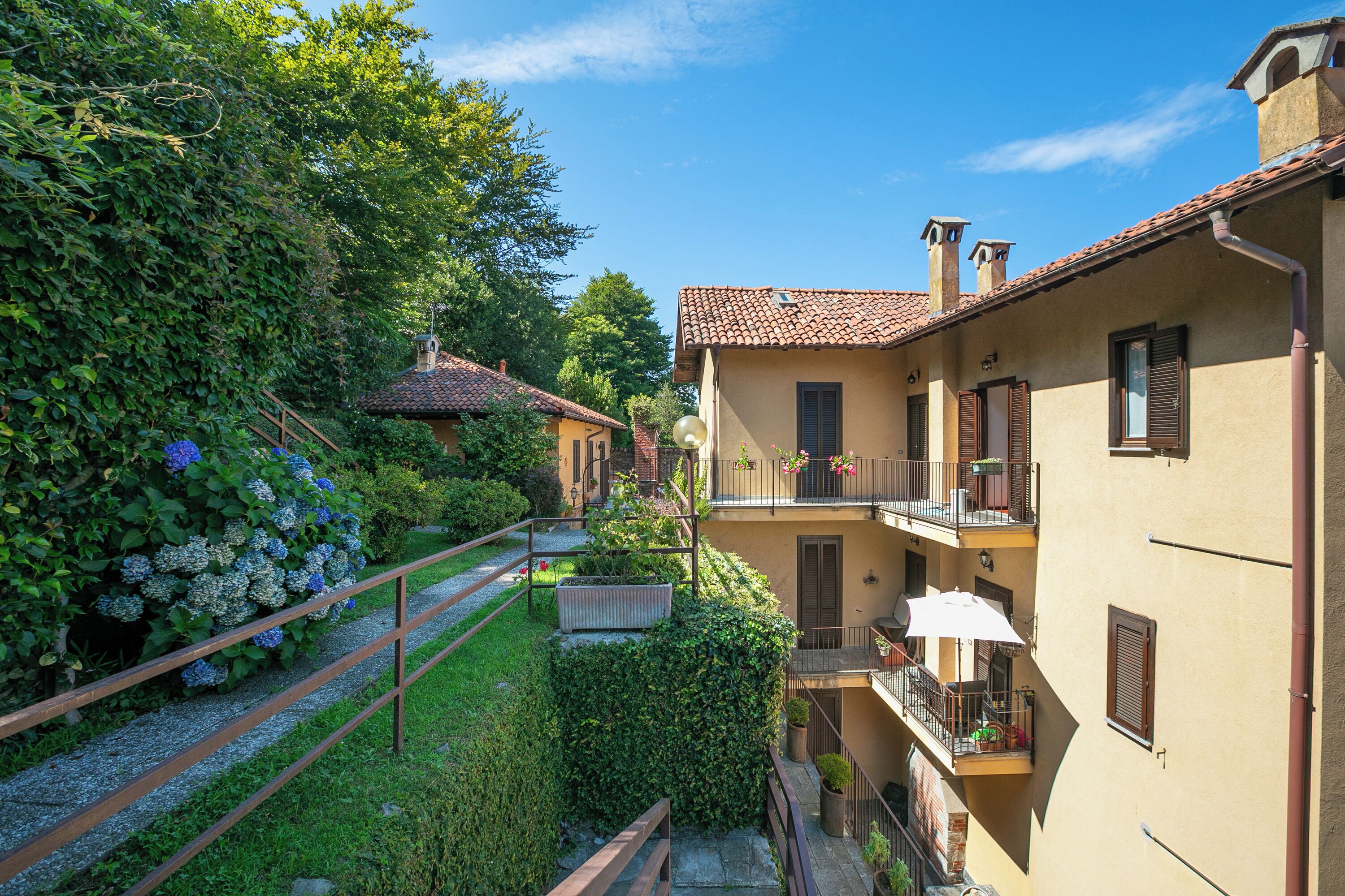A courtyard with a pathway, a hedge, and a building with a balcony.