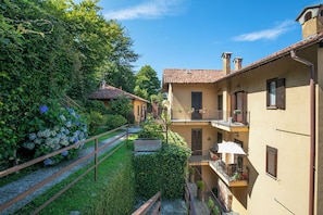 A courtyard with a wooden fence, a small garden with hydrangeas, and a building with a tiled roof and balconies.