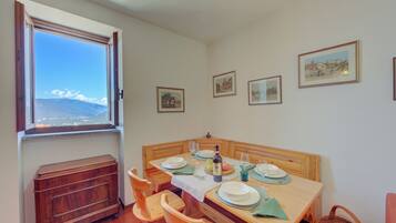 A dining area with a table set for two, wooden chairs, a window with a view of mountains, and framed pictures on the wall.